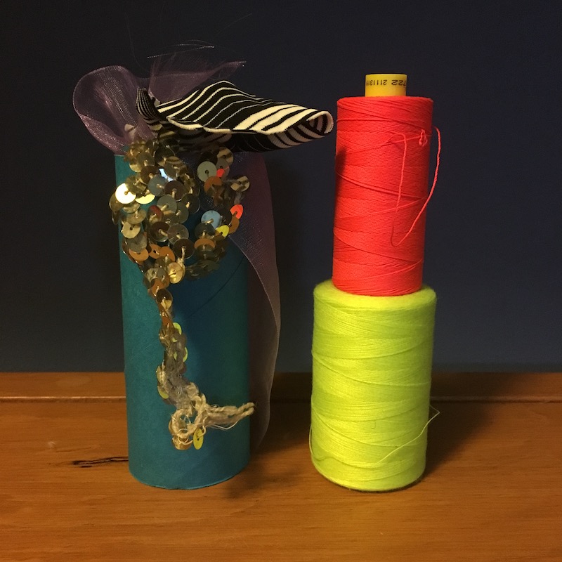 photo of a blue toilet paper tube, two spools of flourescent thread and some silver sequins