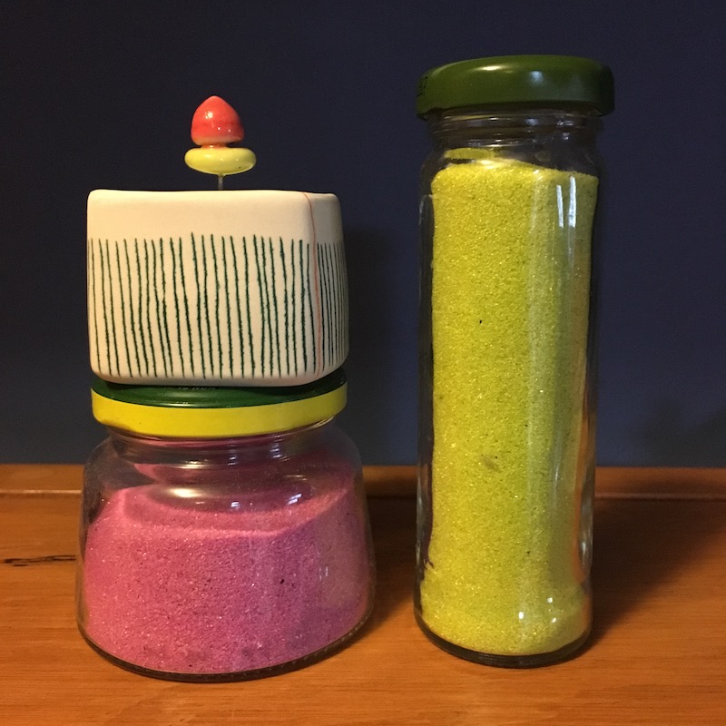 photo of a two jars with colored sand and a striped ceramic container